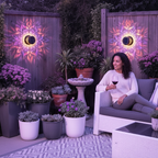 A woman smiles while holding a wine glass on a patio at dusk, illuminated by solar-powered GloPetal lights casting a soft lav